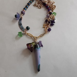 May include: A purple and green glass pendant necklace with a variety of beads and charms, including a crescent moon, stars, and flowers.