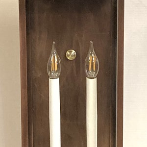 May include: A brown metal wall sconce with two clear glass candle-shaped bulbs and gold accents.