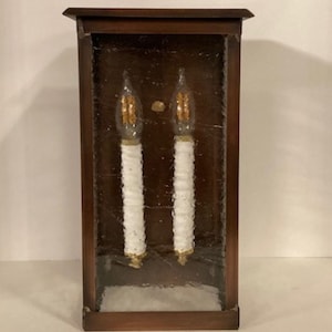 May include: A brown wooden wall sconce with a glass front and two white candle-shaped light bulbs.