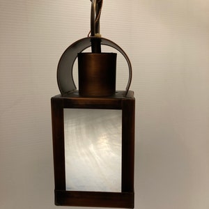 May include: A brown metal hanging lantern with a white frosted glass panel. The lantern has a decorative curved top and a chain for hanging.