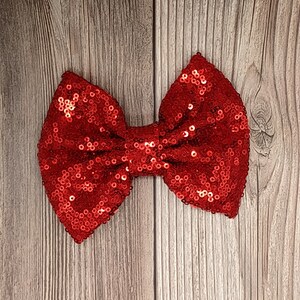 May include: A large red bow made of sequins. The bow is on a wood background.