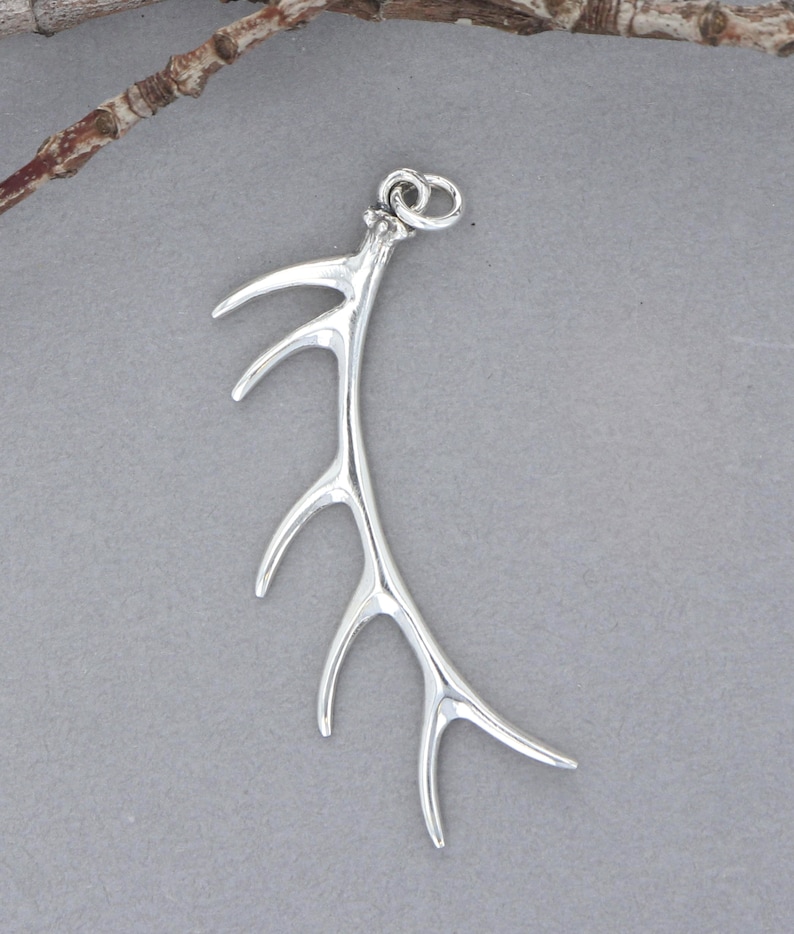 May include: A silver pendant shaped like an antler with a loop at the top for attaching a chain.