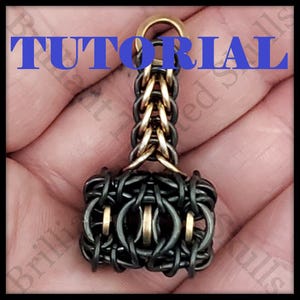 May include: A pendant in the shape of a hammer, made from interwoven black and gold-coloured metal rings. The word "TUTORIAL" is superimposed in blue. The pendant is held in a hand.