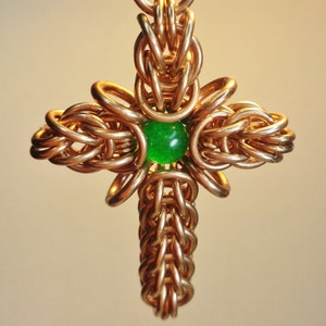 May include: A gold metal cross pendant with a green gemstone in the centre.