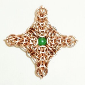 May include: A copper-colored metal pendant in the shape of a four-pointed star with a green gemstone in the center.
