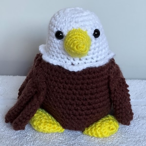 May include: A crocheted bald eagle plush toy with brown feathers, a white head, yellow beak, and black eyes.