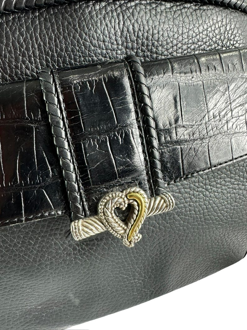 May include: Black leather handbag with a textured finish and a silver and gold heart-shaped clasp. The bag features a braided leather strap detail and a crocodile-embossed flap. The overall design is elegant and classic.