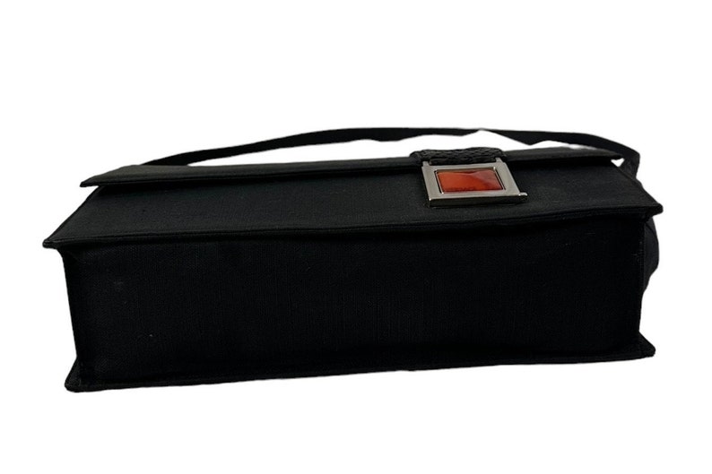 May include: Black rectangular handbag with a flap closure and a shoulder strap. The bag features a silver-toned clasp with a rectangular, orange-red accent. The bag is made of a textured fabric.