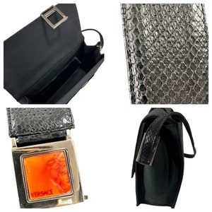 May include: Black handbag with a rectangular shape. The bag features a textured, snake-like pattern on the flap and strap. A silver-toned buckle with an orange and red design and the Versace logo is visible.