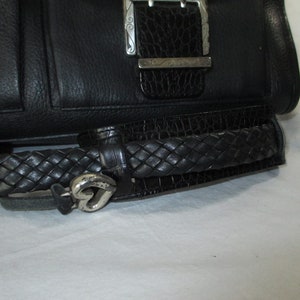 May include: Black leather handbag with a braided strap and a silver heart-shaped charm. The bag has a silver buckle with an intricate design.