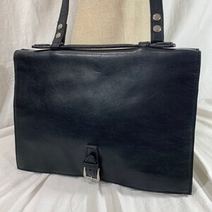 Könnte beinhalten: Eine schwarze Ledertasche mit einer silbernen Schnalle und einem silbernen Riemen mit Nieten. Die Tasche hat einen Klappverschluss.