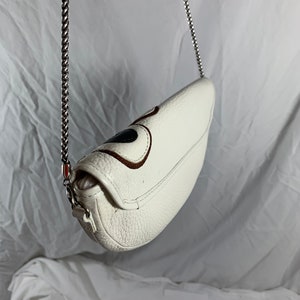 May include: White leather crossbody bag with a silver chain strap and a brown and black design on the front.