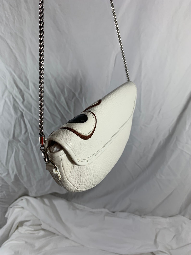 May include: White leather crossbody bag with a silver chain strap and a brown and black design on the front.