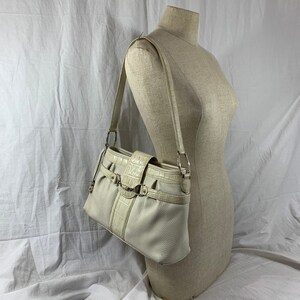 May include: A white leather shoulder bag with a crocodile embossed design and silver hardware. The bag has a flap closure with a buckle and a chain strap.