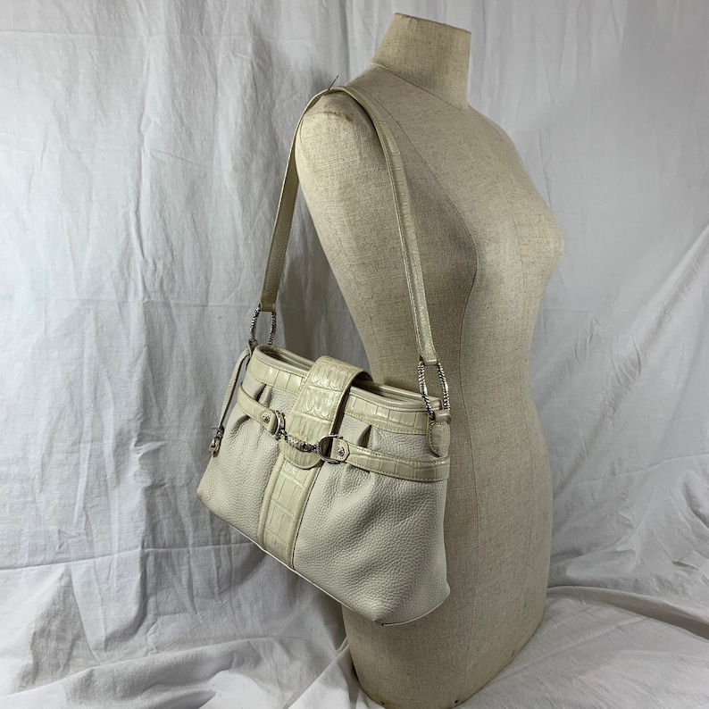 May include: A white leather shoulder bag with a crocodile embossed design and silver hardware. The bag has a flap closure with a buckle and a chain strap.