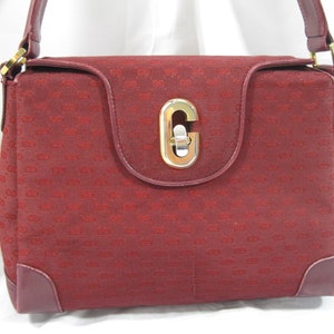 May include: A burgundy shoulder bag with a gold-toned GG monogram pattern and a large gold-toned C-shaped clasp.