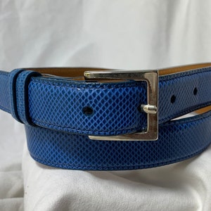 Peut inclure: Une ceinture en cuir bleu avec une boucle argentée. La ceinture a un motif texturé en forme de diamant.