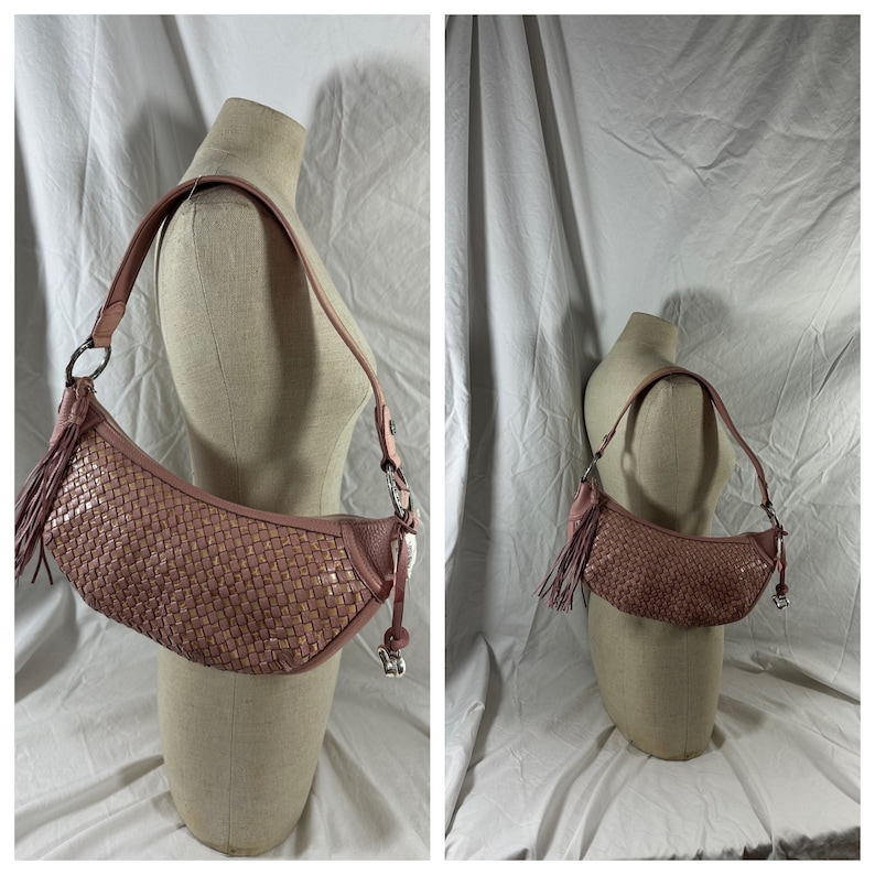 May include: A dusty rose-colored shoulder bag with a woven design. The bag features a curved shape, a long strap, and a tassel detail. The bag is displayed on a mannequin against a white backdrop.
