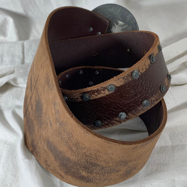 May include: A brown leather belt with metal studs and a distressed finish. The belt is folded in half and the buckle is not visible.