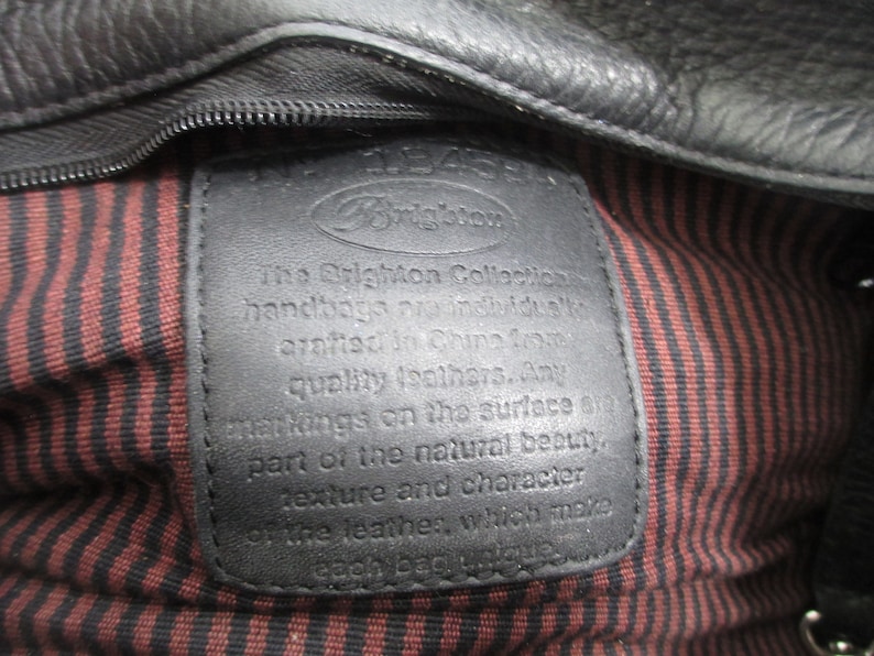 May include: Close-up of a black leather tag with the text "The Brighton Collection handbags are individually crafted in China from quality leathers. Any markings on the surface are part of the natural beauty, texture and character of the leather, which make each bag unique."