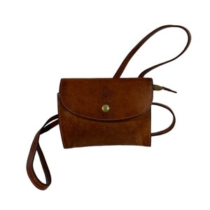 May include: A brown leather crossbody bag with a flap closure and a gold button. The bag has a long adjustable strap.