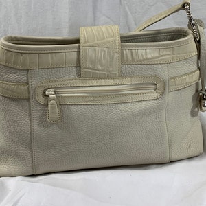 May include: A white leather handbag with a crocodile embossed design. The bag has a zippered pocket on the front and a top handle.