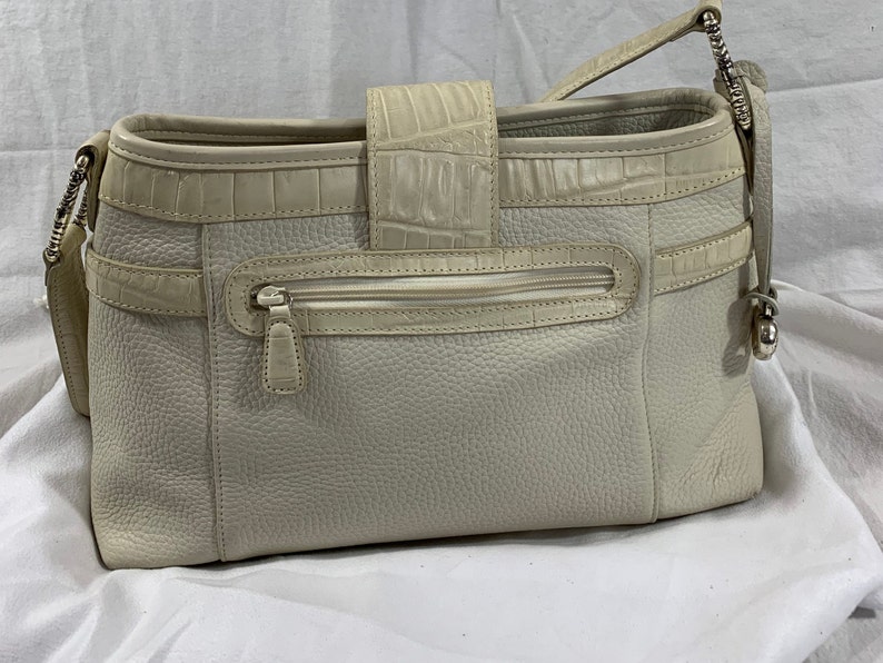 May include: A white leather handbag with a crocodile embossed design. The bag has a zippered pocket on the front and a top handle.