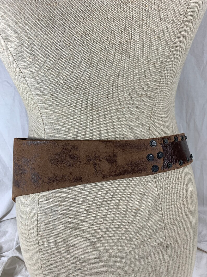 May include: A brown leather belt with metal studs. The belt is worn on a dress form.