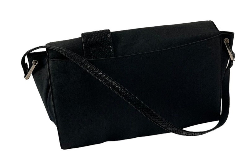 May include: Black messenger bag with a textured flap closure and a woven shoulder strap. The bag has a rectangular shape with a flap that secures with a textured leather strap. The shoulder strap is thin and woven.