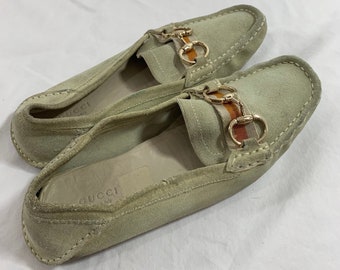Könnte beinhalten: Ein Paar hellgrüne Wildlederschuhe mit goldener Kette und gestreiften Akzenten. Die Schuhe haben ein Gucci-Logo auf der Innensohle.
