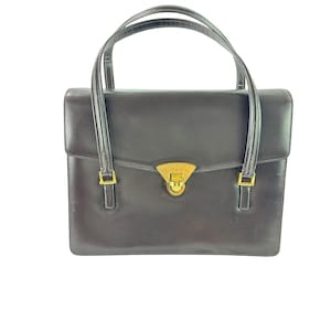 May include: A dark brown leather handbag with two top handles and a rectangular shape. The bag features a gold-colored clasp and gold-colored hardware on the handles. The bag is designed with a structured silhouette.