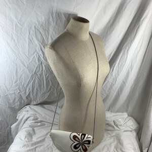 May include: A white leather half-moon shaped crossbody bag with a brown and white floral design and a silver chain strap.