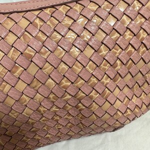 May include: Close-up of a woven leather handbag in a soft pink and tan color scheme. The bag features a basketweave design with a curved top and a subtle texture. The leather appears to be high-quality.