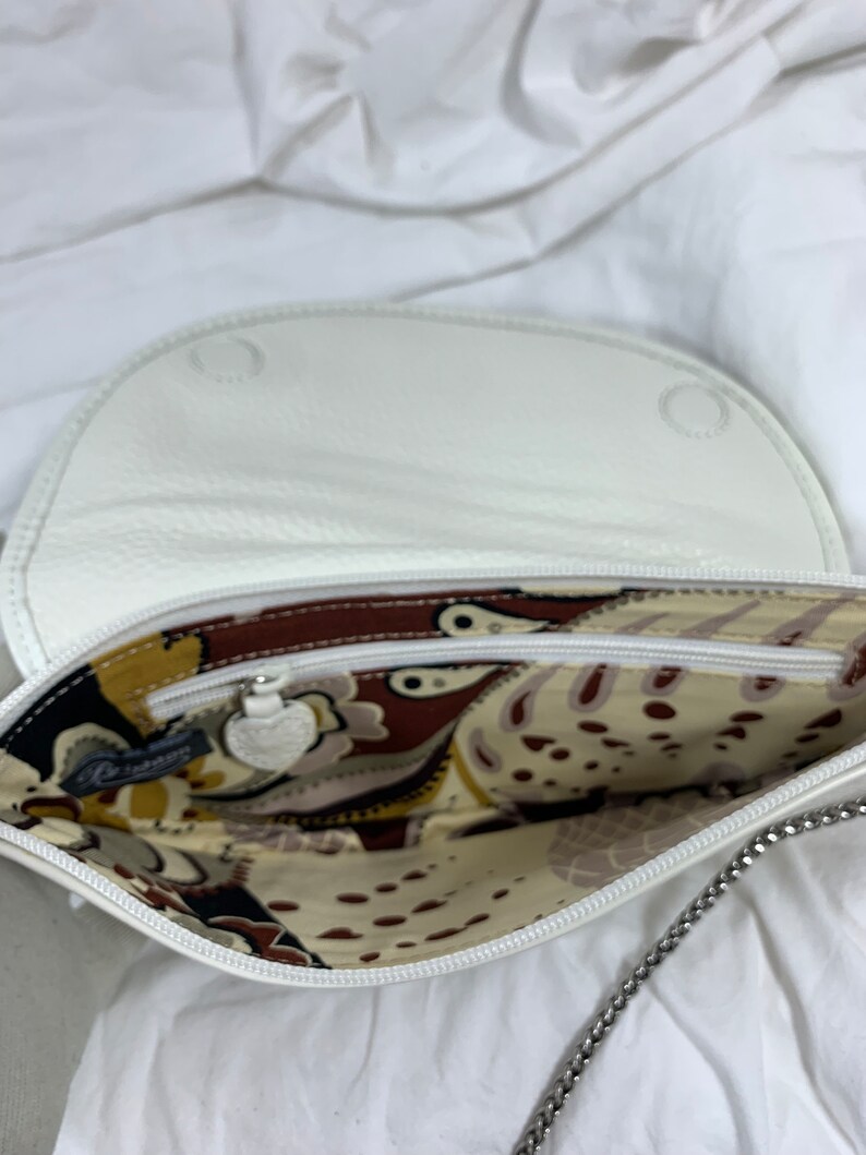 May include: White leather purse with a chain strap and a patterned fabric lining. The purse has a zipper closure and a small metal charm.