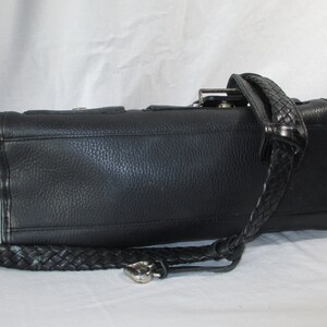 May include: Black leather handbag with a braided strap. The bag has a textured surface and a silver buckle.