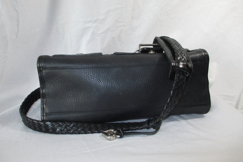 May include: Black leather handbag with a braided strap. The bag has a textured surface and a silver buckle.
