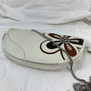 May include: White leather half-moon shaped handbag with a brown, black, and white floral design and a silver chain strap.