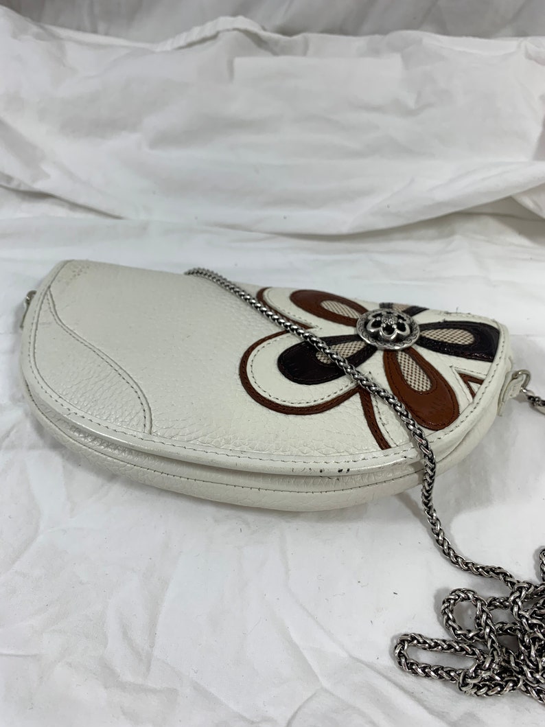 May include: White leather half-moon shaped handbag with a brown, black, and white floral design and a silver chain strap.