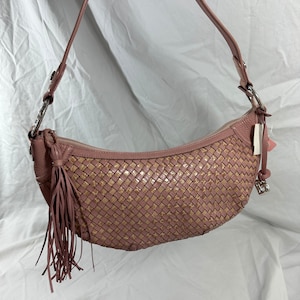 May include: A pink leather shoulder bag with a woven design. The bag features a crescent shape, a long strap, and a tassel. The woven pattern is a mix of pink and tan squares. Silver-tone hardware accents the bag.
