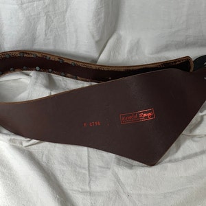 May include: A brown leather belt with a metal buckle and rivets. The belt is stamped with the text "Knotted Rouge" and the number "M 6795".