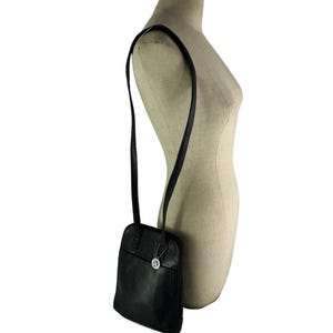 May include: Black leather shoulder bag with a long strap. The bag has a rectangular shape with rounded corners and a small silver charm. The strap is thin and appears to be adjustable. The bag is displayed on a mannequin.