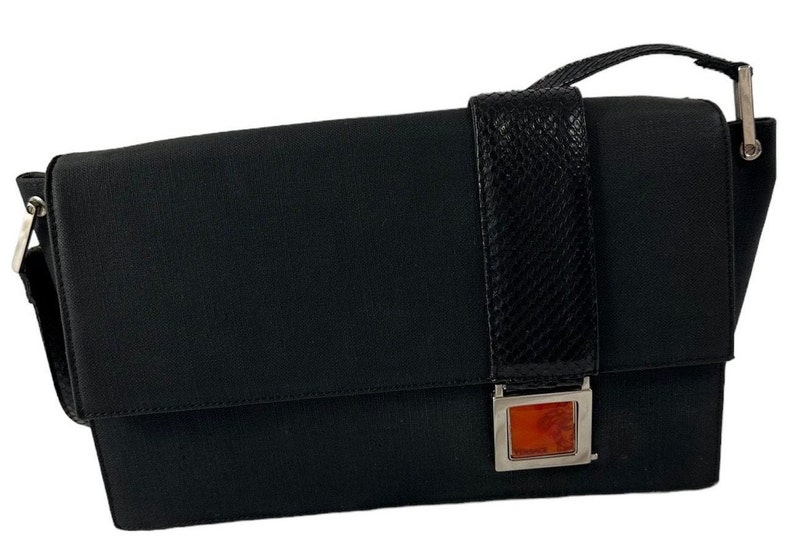 May include: Black messenger bag with a flap closure. The bag features a textured black strap and a decorative rectangular clasp with an orange-red center. The bag has a shoulder strap and a silver-colored metal buckle.