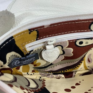 May include: The inside of a white leather purse with a paisley patterned lining. The purse has a zipper closure and a small leather tag that says "Brighton".