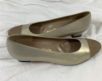 May include: A pair of beige leather pumps with a woven brown leather toe cap. The shoes have a low heel and are made by the brand "Salvatore Ferragamo".