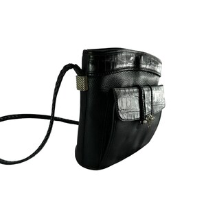 May include: Black leather crossbody bag with a textured flap pocket and a braided strap. The bag features a silver-toned clasp and a crocodile-textured accent on the flap and top.