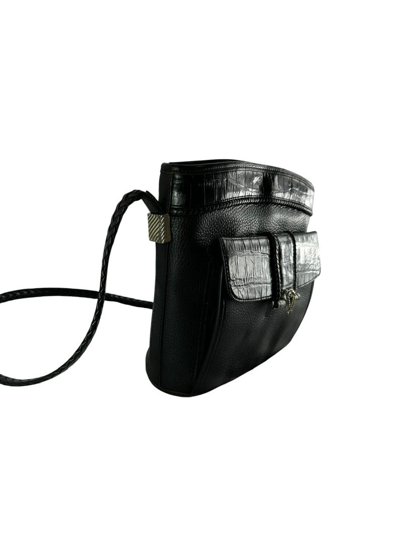 May include: Black leather crossbody bag with a textured flap pocket and a braided strap. The bag features a silver-toned clasp and a crocodile-textured accent on the flap and top.