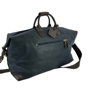 May include: A navy blue leather travel bag with brown leather detailing. The bag features a top handle, a shoulder strap, and a zipped pocket. A luggage tag is attached to the handle.