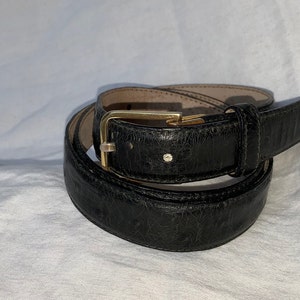 Op de afbeelding: Een zwarte leren riem met een gouden gesp. De riem is opgerold en de gesp is zichtbaar.