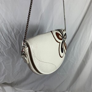 May include: White leather handbag with a silver chain strap and a brown and white floral design.