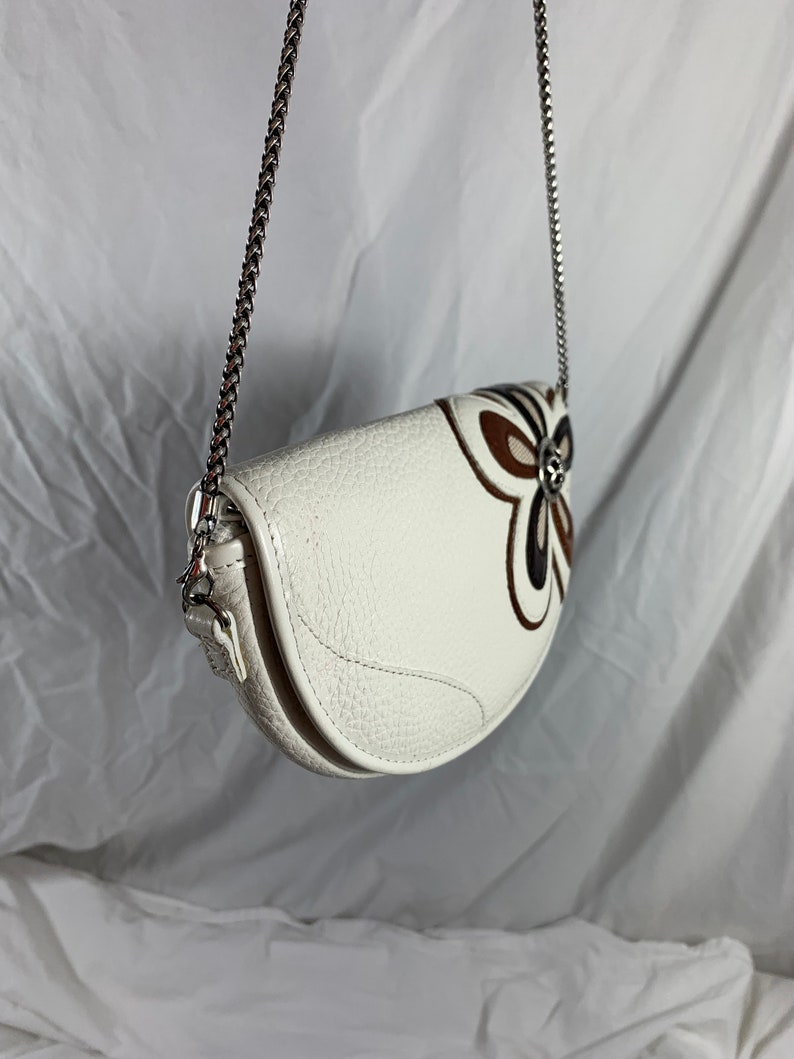May include: White leather handbag with a silver chain strap and a brown and white floral design.